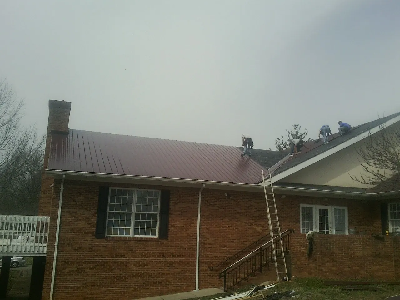 Crew setting red metal roofing panels on a brick home in Nicktown