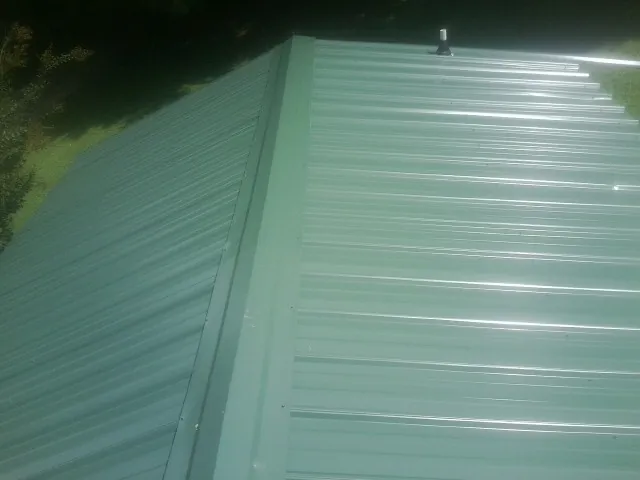 New green metal panels meeting at the ridge of a roof — Flat Roof Repair work by our crew in Nicktown