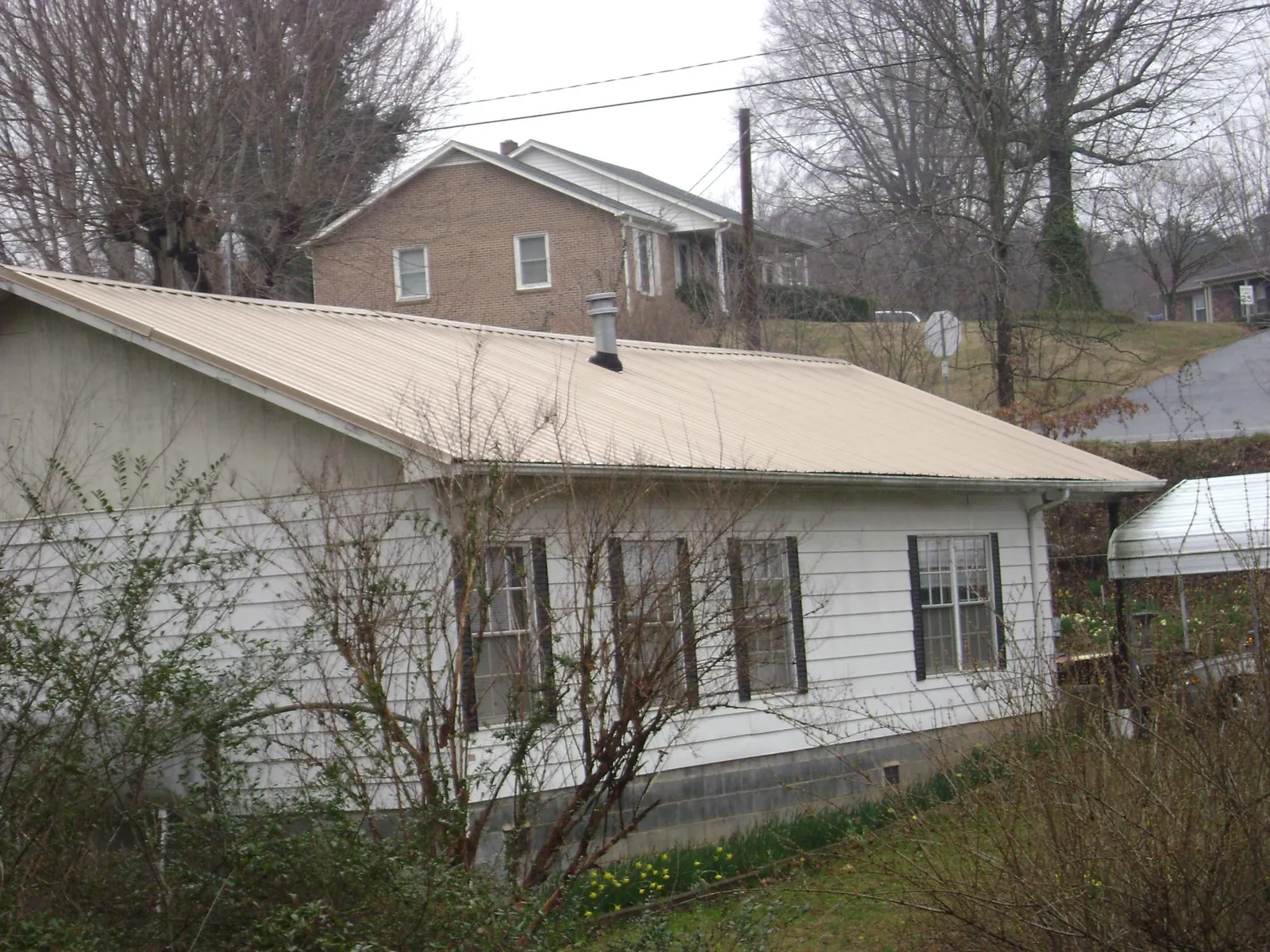Tan metal roof on a white sided house set into a hillside — Commercial Roofing by Roofing Brothers in Nicktown